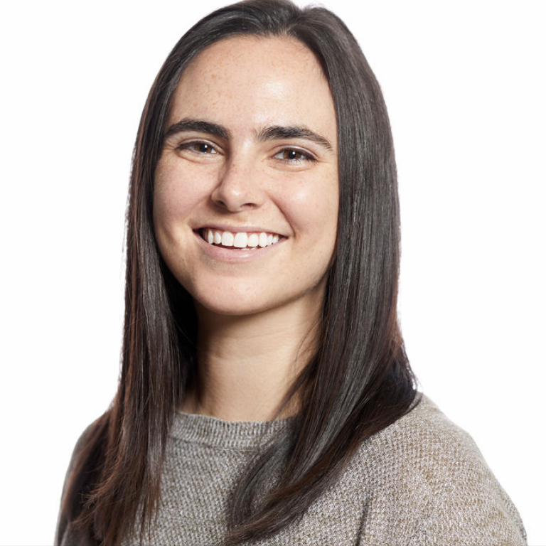 A smiling person with straight dark hair wearing a light grey knit top against a plain white background.
