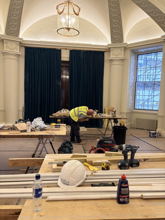 Dining room during refurbishment, with a worker surrounded by tools, timber and building materials.